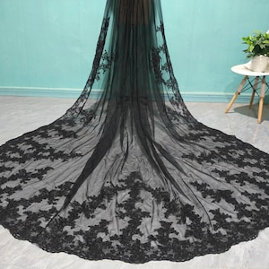 May include: A black tulle wedding veil with delicate floral lace embroidery. The veil is long and flowing, with a scalloped edge.