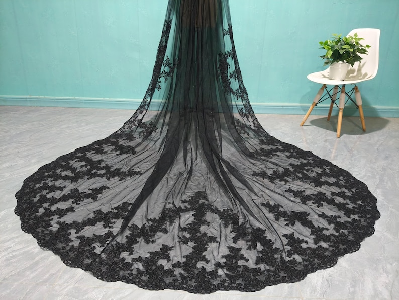 May include: A black tulle wedding veil with delicate floral lace embroidery. The veil is long and flowing, with a scalloped edge.