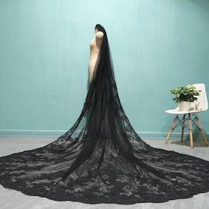 May include: A black lace wedding veil with a long train. The veil is made of delicate lace and has a scalloped edge.