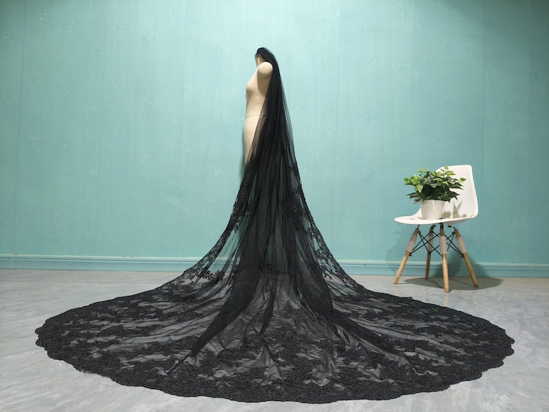 May include: A black lace wedding veil with a long train. The veil is made of delicate lace and has a scalloped edge.