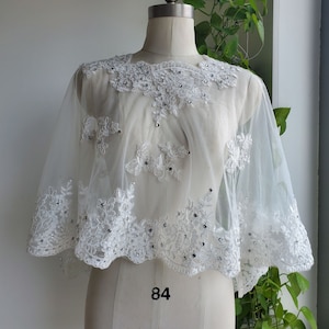 Könnte beinhalten: Weiße Braut-Kappe aus Spitze mit einem gewellten Rand und silbernen Verzierungen. Die Kappe befindet sich auf einer weißen Kleiderpuppe.