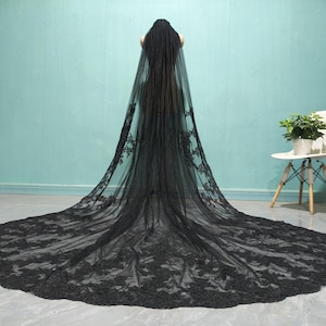 May include: A black lace wedding veil with a long train. The veil is made of delicate lace and has a scalloped edge.