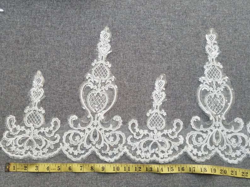 May include: White lace trim with a delicate floral pattern. The trim features a repeating design of hearts and swirls. The trim is approximately 22 inches long.