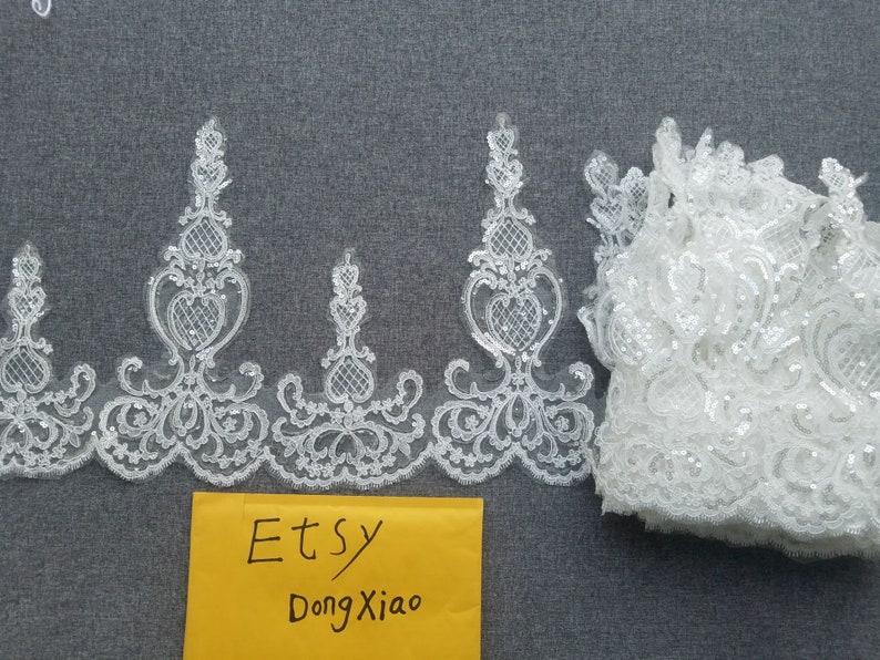 May include: White lace trim with a delicate floral pattern and sequins. The trim is folded and displayed on a gray surface. The text "Etsy DongXiao" is written on a yellow envelope.