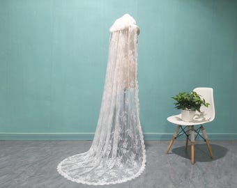 May include: A white lace bridal veil with a scalloped edge. The veil is draped over a mannequin and is displayed against a light blue background.