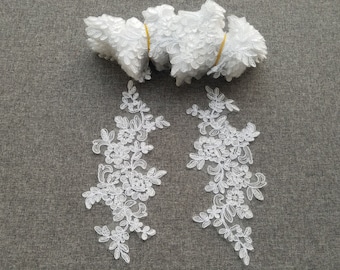 May include: Two white lace appliques with floral designs. The appliques are on a gray background.