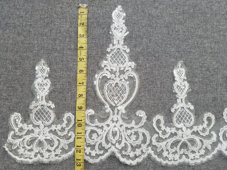 May include: White lace trim with a delicate floral pattern and sequins. The trim is approximately 13 inches long.