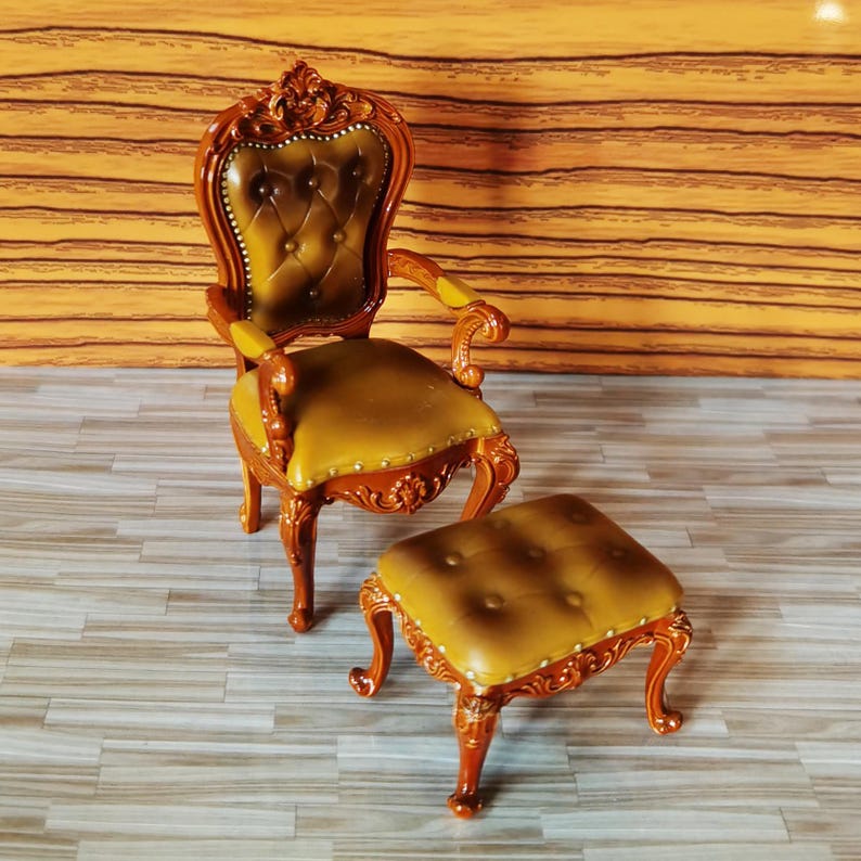May include: A brown wooden armchair with a tufted brown leather seat and a matching brown wooden footstool. The chair and footstool have ornate carvings and a classic design.