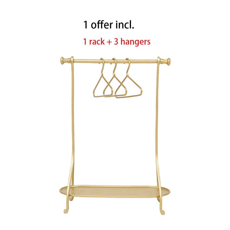 May include: A gold-colored metal clothing rack with a horizontal bar, a bottom shelf, and three matching gold-colored hangers. The text above the rack reads: 1 offer incl. 1 rack + 3 hangers. The structure features curved side supports.