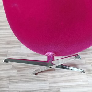 Pu&ograve; includere: Una sedia a forma di uovo rosa brillante con una base cromata. La sedia &egrave; realizzata in un tessuto morbido e soffice e ha un design elegante e moderno.