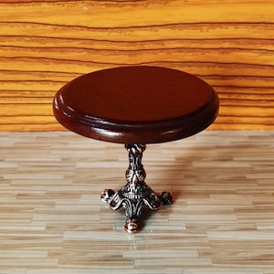 May include: A miniature wooden table with a dark brown top and a decorative metal base with a scrolled design. The table has three legs and is approximately 4 inches in diameter.