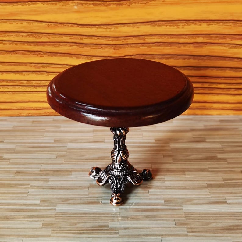 May include: A miniature wooden table with a dark brown top and a decorative metal base with a scrolled design. The table has three legs and is approximately 4 inches in diameter.
