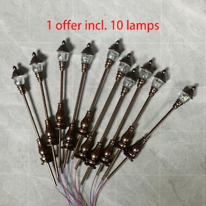 Puede incluir: Diez farolas de bronce en miniatura con globos de cristal transparente y pequeñas luces LED. Las lámparas tienen un diseño clásico con bases decorativas y están conectadas por cables. El texto "1 offer incl. 10 lamps" es visible.