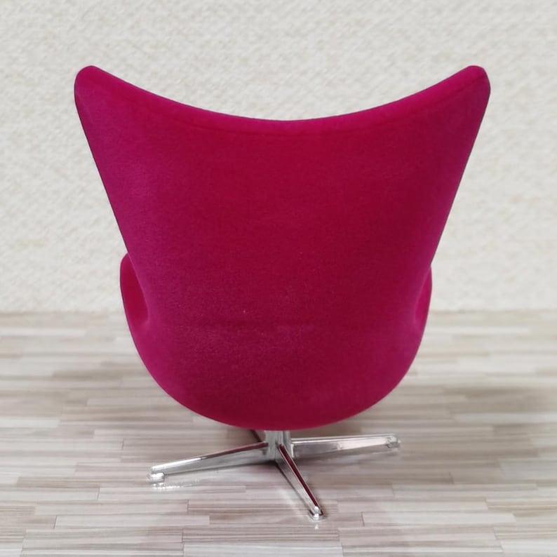 Pu&ograve; includere: Una sedia a forma di uovo di colore rosa brillante con una base girevole in cromo. La sedia &egrave; rivestita in un tessuto morbido e soffice.