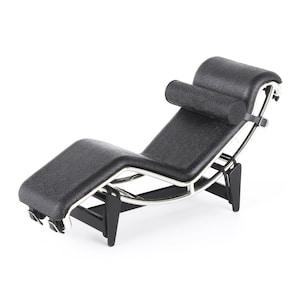 Könnte beinhalten: Eine schwarze Lederliege mit einem verchromten Gestell und einer schwarzen zylindrischen Kopfstütze. Die Liege ist abgewinkelt und hat ein schlankes, modernes Design.