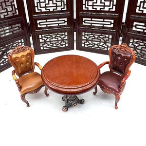 May include: A miniature wooden table set with two chairs. The table has a round top and a carved base. The chairs have brown leather upholstery and carved wooden frames.