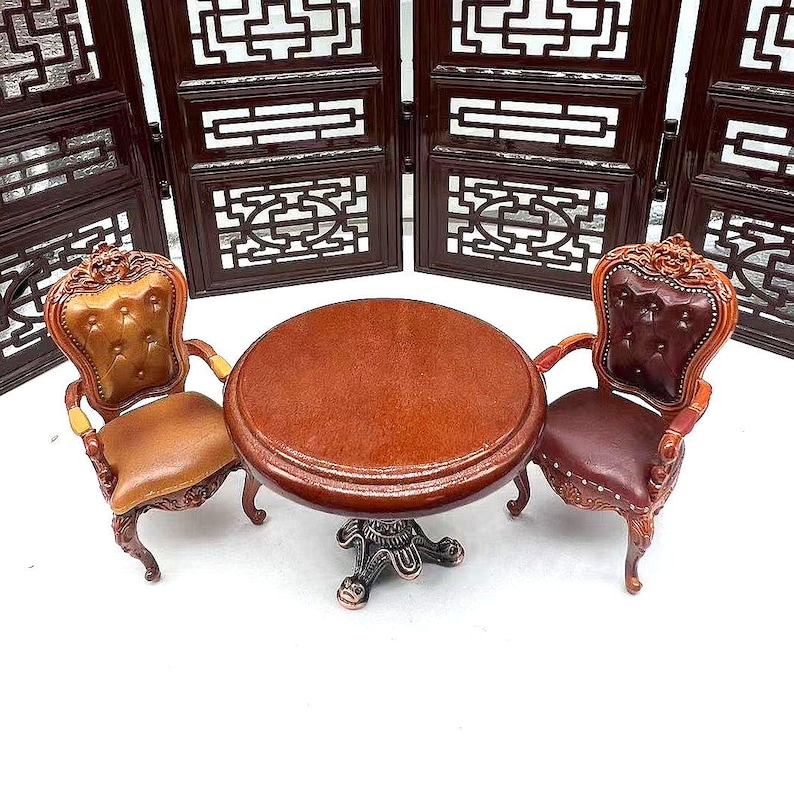 May include: A miniature wooden table set with two chairs. The table has a round top and a carved base. The chairs have brown leather upholstery and carved wooden frames.