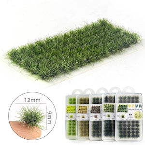 Könnte beinhalten: Ein rechteckiger Flecken grünes Modellgras, verpackt in klarem Kunststoff, mit einer Nahaufnahme, die einen 12 mm hohen Büschel zeigt. Mehrere kleine Behälter mit saisonalen Grastuffs sind ebenfalls sichtbar, jeder mit einem anderen Grünton.
