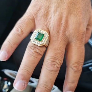 Op de afbeelding: Een gouden ring met een grote smaragdgroene edelsteen omringd door kleinere heldere edelstenen.