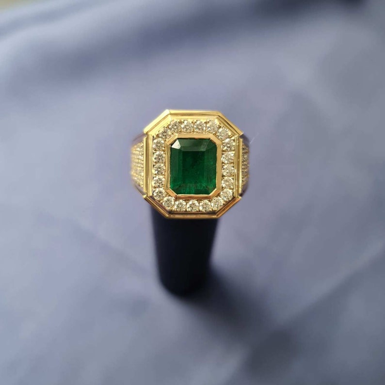 Op de afbeelding: Een gouden ring met een grote smaragdgroene edelsteen omringd door kleinere heldere edelstenen.