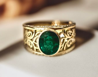 May include: A gold ring with a large oval emerald gemstone surrounded by a band of smaller diamonds. The ring has a delicate, intricate design with a filigree pattern.