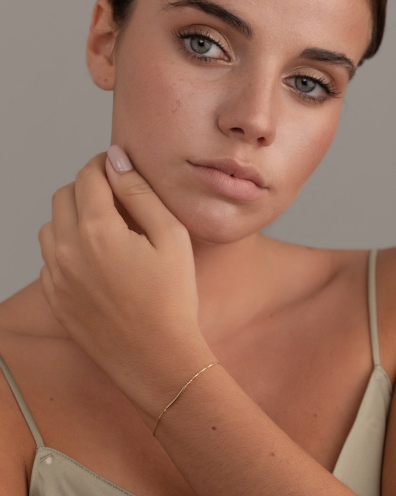 May include: A delicate gold chain bracelet with a simple design. The bracelet is worn on a person's wrist.
