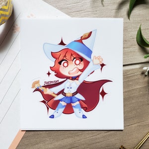 Peut inclure: Un autocollant représentant un personnage de dessin animé avec des cheveux roux, portant un chapeau bleu et blanc, une robe blanche et une cape rouge. Le personnage tient une baguette bleue et dorée et est entouré d'étoiles scintillantes. Le texte "JUSTMISHY" est imprimé sur l'autocollant.