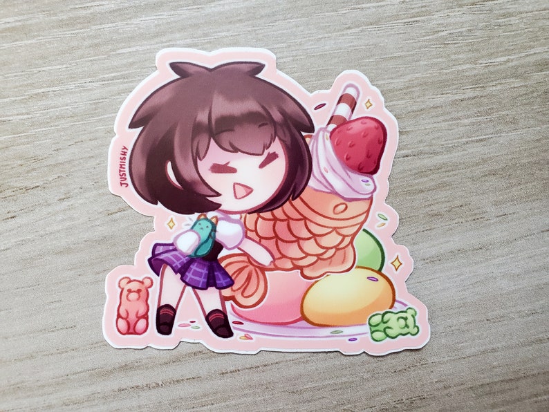 Puede incluir: Una pegatina con un personaje de dibujos animados con cabello casta&ntilde;o, que lleva una camisa blanca y una falda de cuadros morados, sosteniendo una criatura verde y azul. El personaje est&aacute; de pie junto a un gran postre colorido con una fresa en la parte superior. El postre est&aacute; rodeado de chispas y otros peque&ntilde;os caramelos.