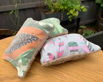 May include: Three colorful kitchen scrubbers with a mesh outer layer and a soft, brown terry cloth backing. The scrubbers feature different patterns: a papaya, a geometric design, and a floral design.