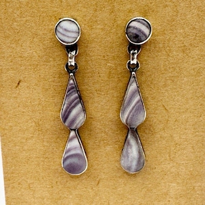 May include: A pair of silver-toned drop earrings. Each earring features a small, round stud and a teardrop-shaped dangle. The dangles have a marbled pattern in shades of purple and white. The earrings are displayed against a tan background.