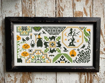 Op de afbeelding: Een zwart ingelijst kruissteek-sampler met een Halloween-thema. Het ontwerp bevat verschillende motieven, waaronder pompoenen, vleermuizen, katten, een heks en een spookachtige boom. De kleuren zijn zwart, groen en oranje.
