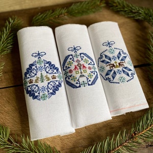 May include: Three white fabric panels with blue and green embroidered Christmas ornaments. Each ornament features a different design with snowflakes, trees, and other festive elements.