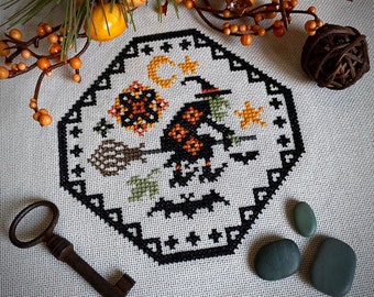 May include: Black and white cross-stitch pattern of a witch flying on a broomstick with a cat and stars. The pattern is framed in a black hexagon with white stars.