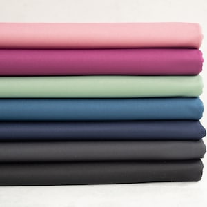 Könnte beinhalten: Stapel von sieben Stoffproben in verschiedenen Farben, darunter rosa, lila, grün, blau und grau.