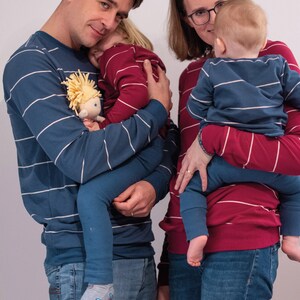 May include: A family of four wearing matching striped pyjamas. The parents are holding their two children, one in each arm. The parents are wearing blue and white striped pyjamas, while the children are wearing red and white striped pyjamas.