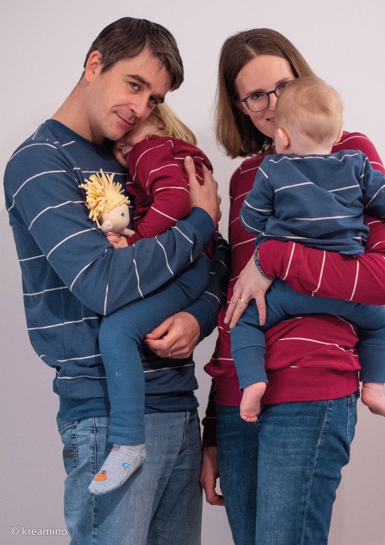 May include: A family of four wearing matching striped pyjamas. The parents are holding their two children, one in each arm. The parents are wearing blue and white striped pyjamas, while the children are wearing red and white striped pyjamas.