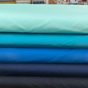 Könnte beinhalten: Fünf Stoffrollen in Blautönen, Türkis und Hellblau. Der Stoff ist glatt und seidig.