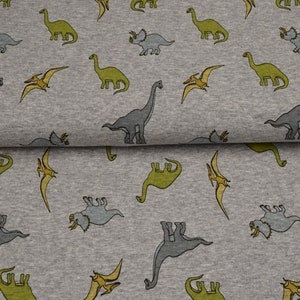 Könnte beinhalten: Grauer Stoff mit einem sich wiederholenden Muster aus grünen, grauen und gelben Dinosauriern. Die Dinosaurier umfassen einen Triceratops, einen Stegosaurus und einen Pterodactylus.