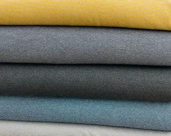May include: Five rolls of striped fabric in different colors. The fabric is stacked on top of each other. The colors are yellow, dark blue, gray, light blue, and white.