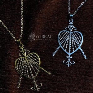 Könnte beinhalten: Zwei silberne und goldene Halsketten mit herzförmigen Anhängern. Die Anhänger sind filigran und zeigen ein Design aus Pfeilen und einem Herzen. Die Halsketten liegen auf einem braunen Hintergrund.