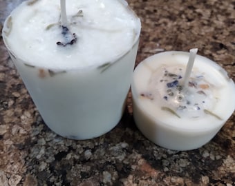 May include: Two white wax candles, one tall cylindrical votive and one shorter round tea light, both featuring embedded dried botanical elements and a single centered white wick, showcasing a smooth, opaque finish with visible floral inclusions.