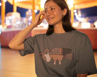 May include: A woman wearing a gray t-shirt with a stylized bird design in brown, pink, and purple. The bird has a large beak and a long tail.