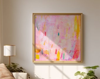 Op de afbeelding: Abstract schilderij in een gouden lijst met roze, gele, blauwe en groene penseelstreken op een witte achtergrond. Het schilderij hangt aan een witte muur in een woonkamer met een bank, een lamp en een plant in een pot.