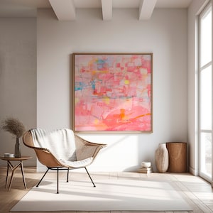 May include: Abstract painting with pink, orange, yellow, and blue hues. The painting is framed in a light wood frame and hangs on a white wall in a living room setting.