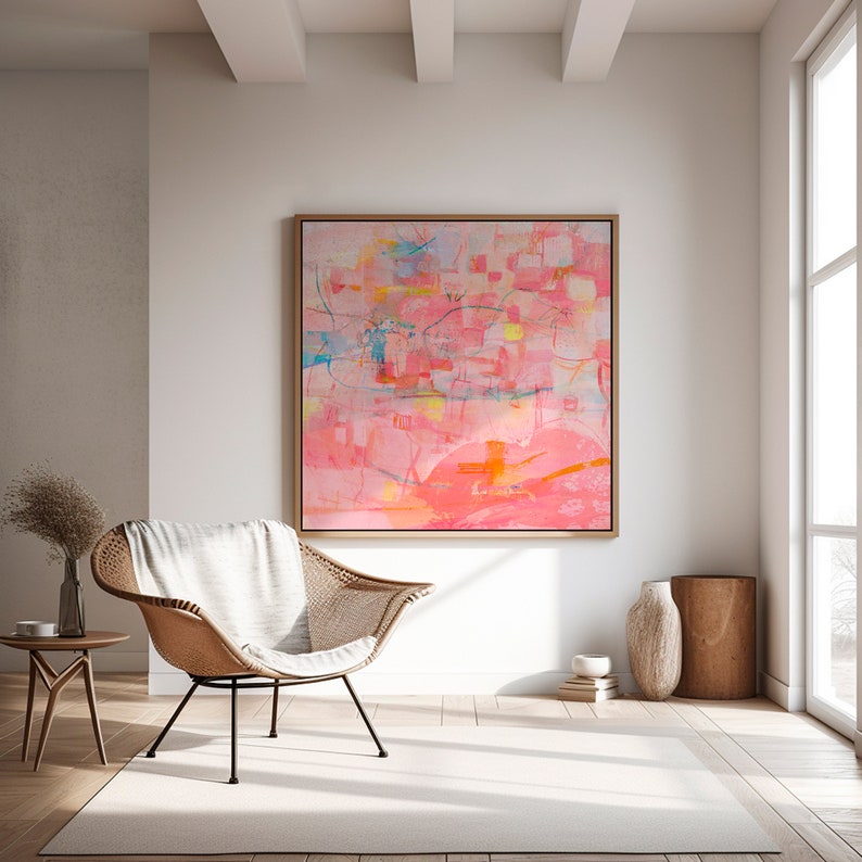 May include: Abstract painting with pink, orange, yellow, and blue hues. The painting is framed in a light wood frame and hangs on a white wall in a living room setting.