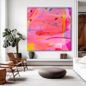 May include: Abstract painting with pink, yellow, blue, and orange colors. The painting is framed and hanging on a white wall in a living room setting.