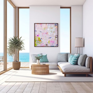 Peut inclure: Un canap&eacute; blanc avec des coussins de couleur bleu clair et gris est plac&eacute; dans un salon avec une grande fen&ecirc;tre donnant sur l'oc&eacute;an. Une table basse en bois se trouve devant le canap&eacute;. Une peinture abstraite encadr&eacute;e aux couleurs rose, verte et bleue est accroch&eacute;e au mur derri&egrave;re le canap&eacute;.