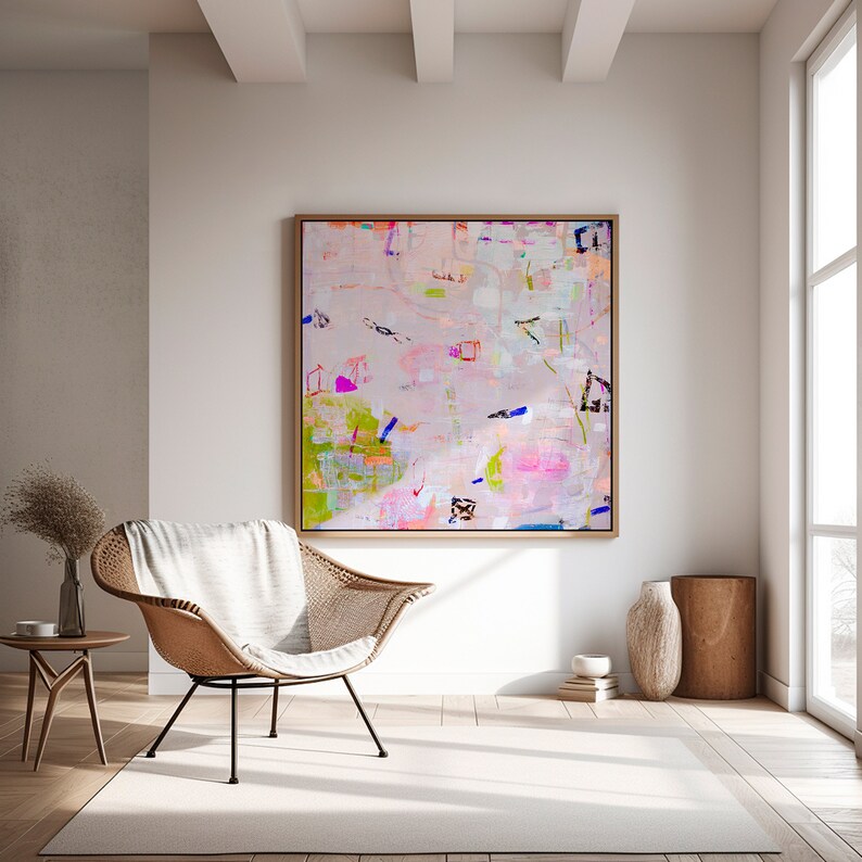 Peut inclure: Peinture abstraite aux couleurs rose, blanche et verte. La peinture est encadr&eacute;e dans un cadre en bois clair et est accroch&eacute;e &agrave; un mur blanc dans un salon. Une chaise en osier et une table en bois sont au premier plan.