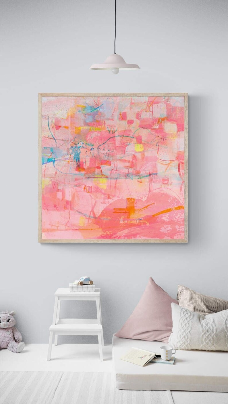 May include: A framed abstract painting with pink, orange, yellow, and blue colors. The painting is hanging on a light gray wall above a white step stool and a white couch with pink and cream pillows.