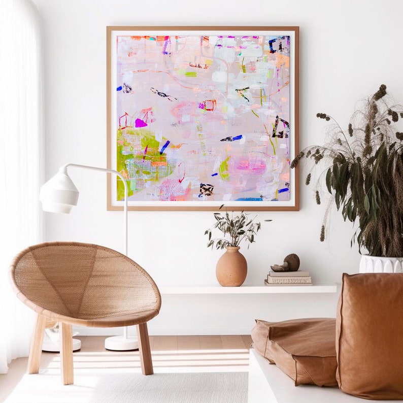 Peut inclure: Une peinture abstraite encadr&eacute;e avec un fond rose clair et des coups de pinceau color&eacute;s dans des tons de bleu, vert, rose et jaune. La peinture est accroch&eacute;e &agrave; un mur blanc au-dessus d'une &eacute;tag&egrave;re blanche avec un vase de fleurs s&eacute;ch&eacute;es et un livre.